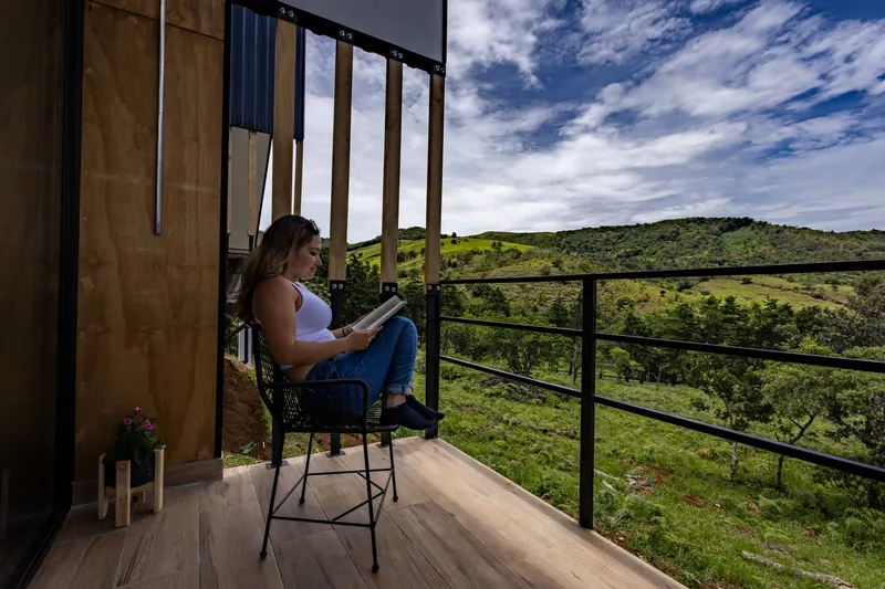 Persona leyendo en la terraza, con el valle verde y el cielo azul de fondo